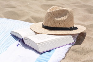 Photo of Beach towel with straw hat and book on sand