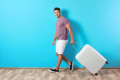 Photo of Young man walking with suitcase on color wall background