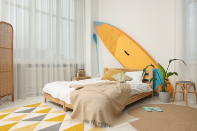 Photo of Large comfortable bed, SUP board and green houseplant in stylish bedroom. Interior design