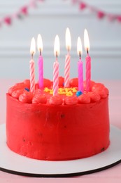 Cute bento cake with tasty cream and burning candles on pink wooden table