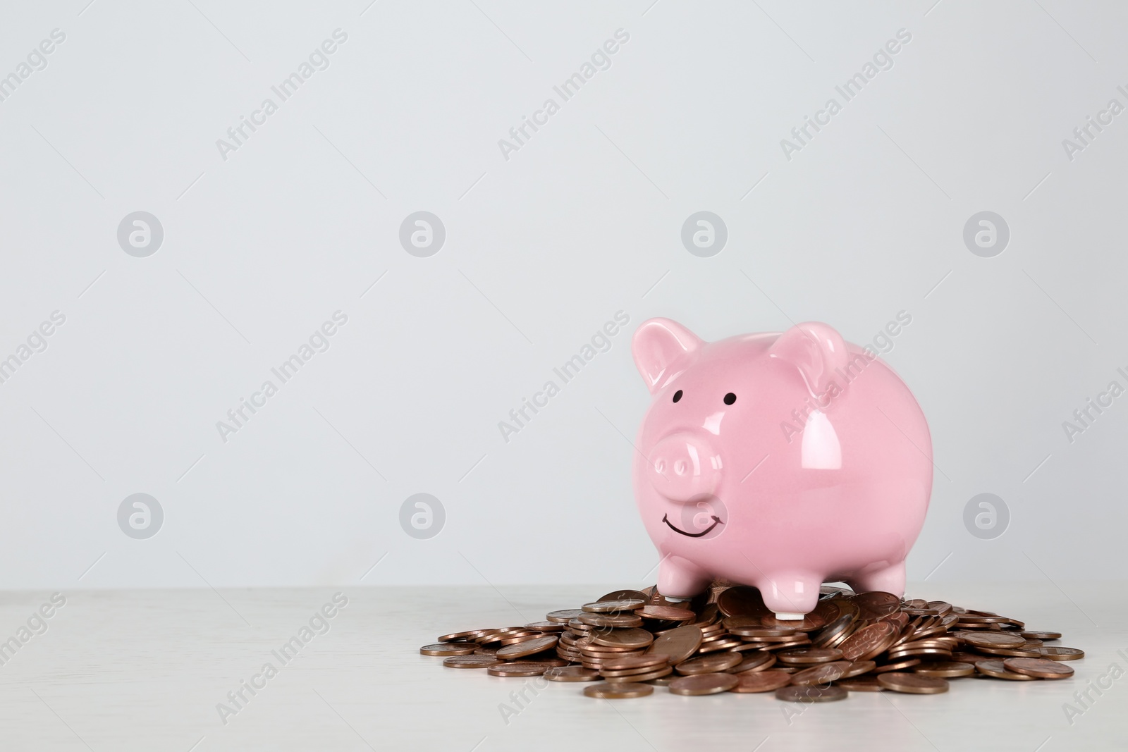 Photo of Piggy bank and coins on table against white background. Space for text