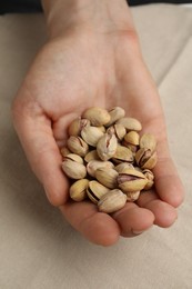 Woman holding tasty roasted pistachio nuts at table, above view