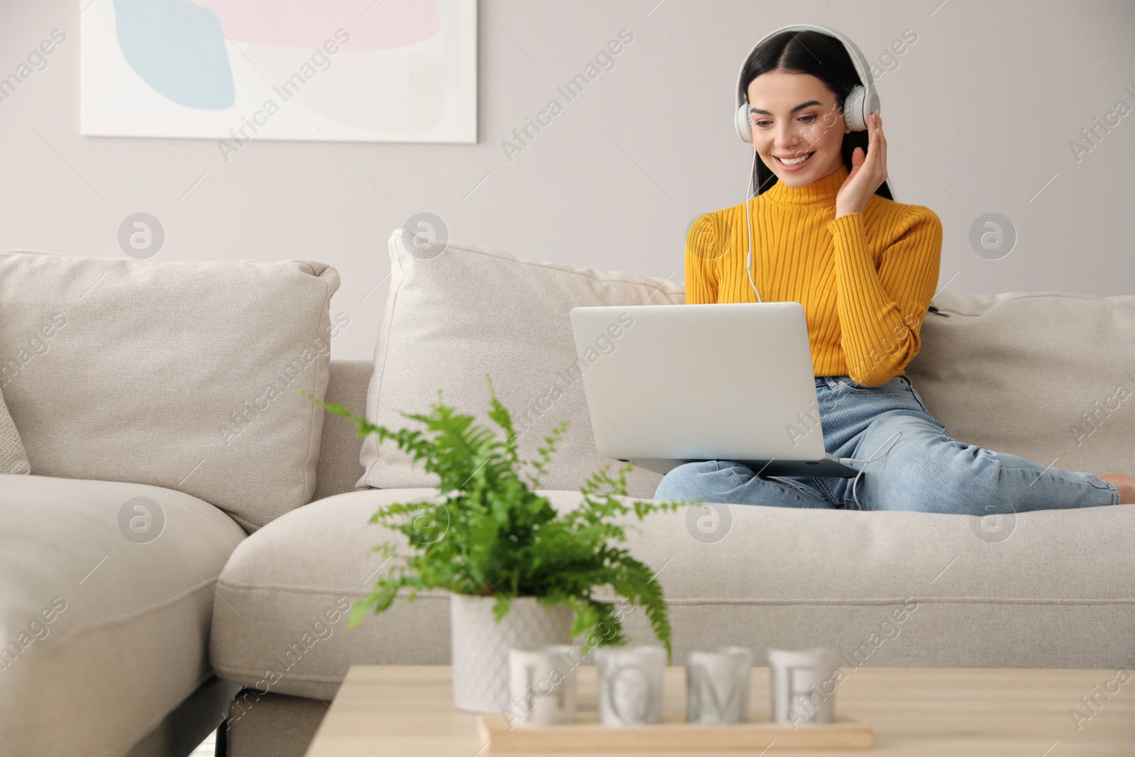 Photo of Woman with laptop and headphones sitting on sofa at home