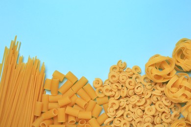 Different types of pasta on light blue background, flat lay. Space for text