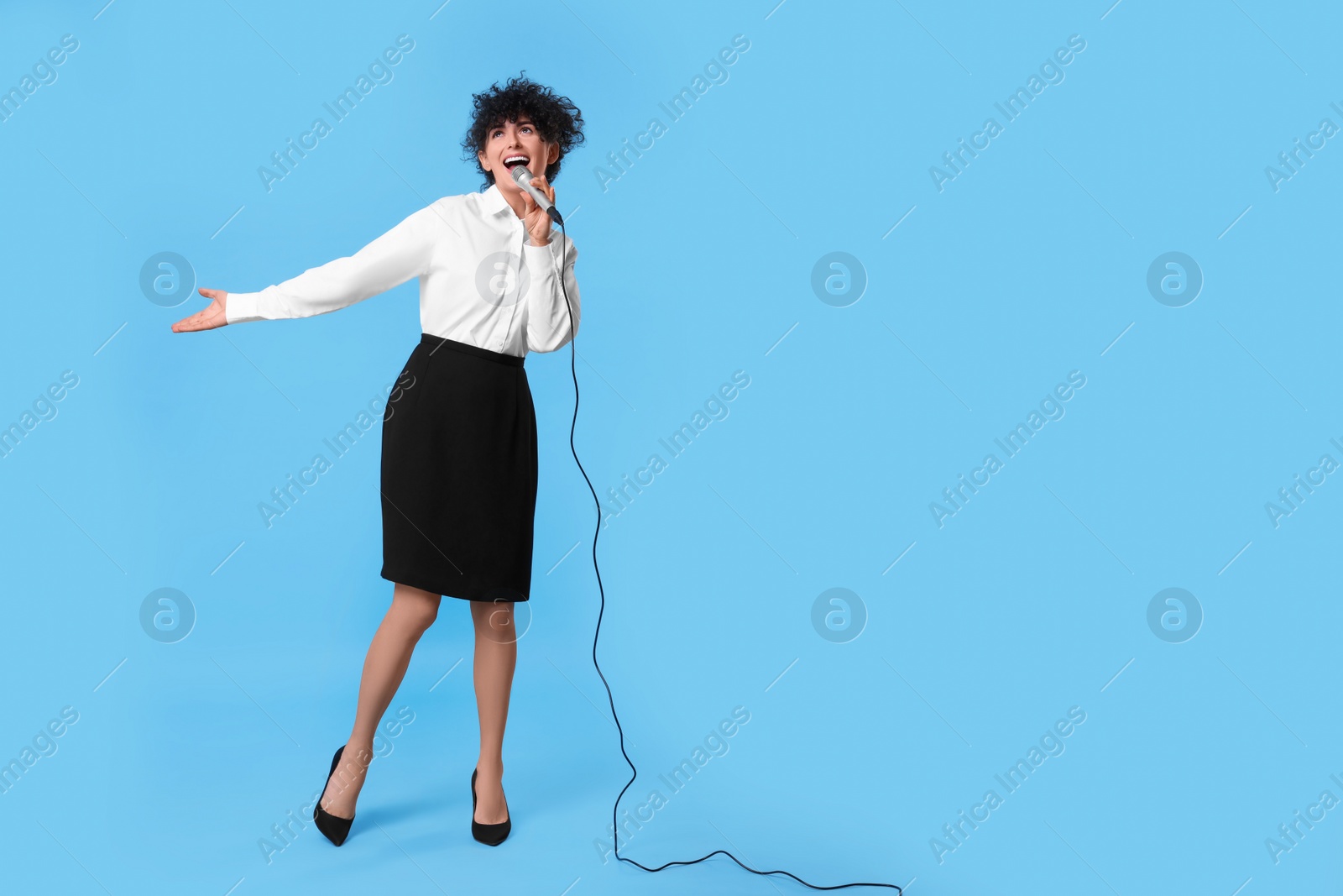 Photo of Beautiful young woman with microphone singing on light blue background