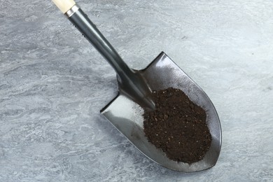 Photo of Metal shovel with fertile soil on gray textured surface, above view