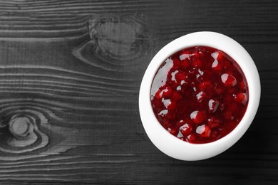Photo of Fresh cranberry sauce in bowl on black wooden table, top view. Space for text