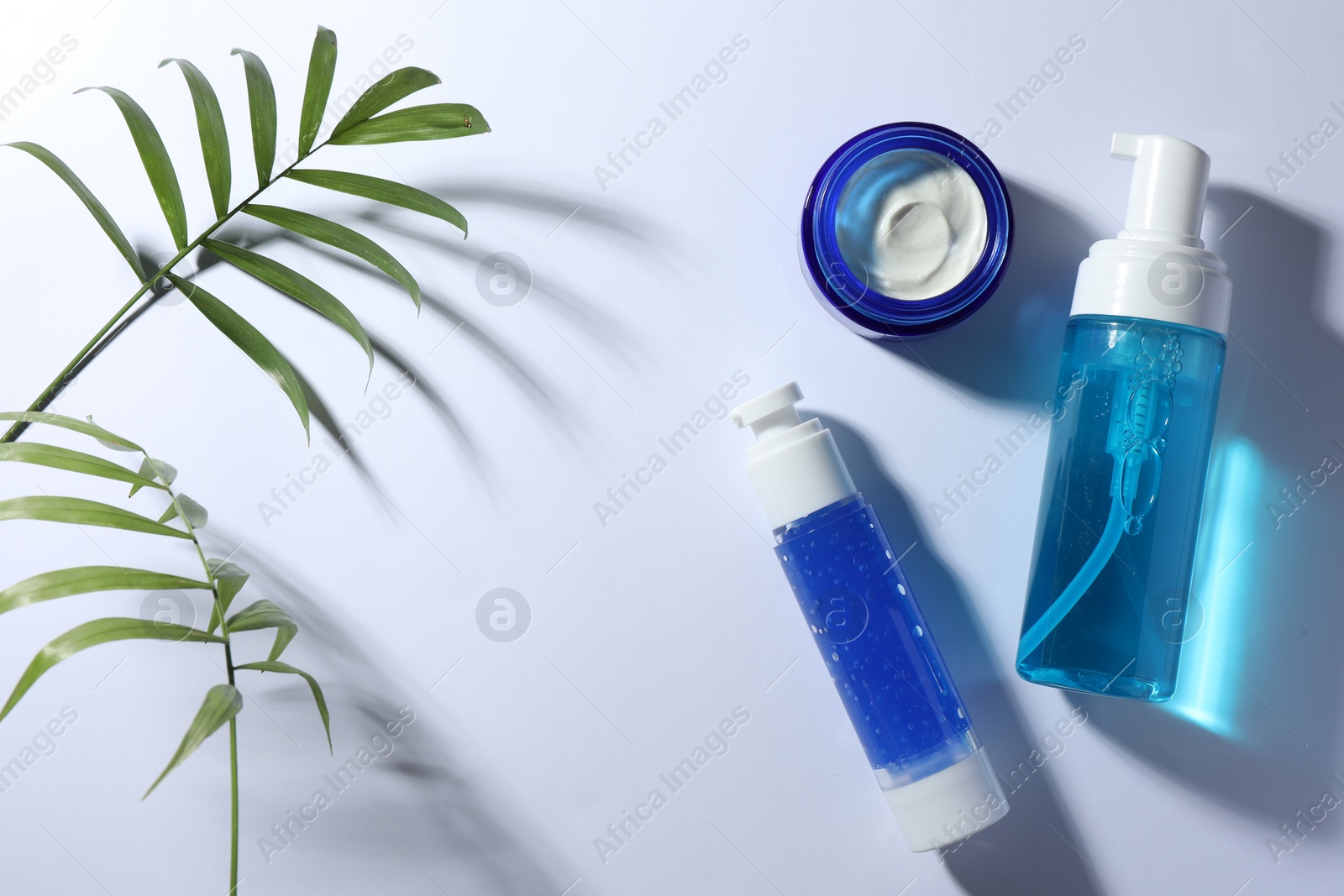 Photo of Set of cosmetic products and green leaves on white background, flat lay