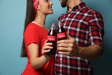Photo of MYKOLAIV, UKRAINE - JANUARY 27, 2021: Young couple holding bottles of Coca-Cola against light blue background, closeup
