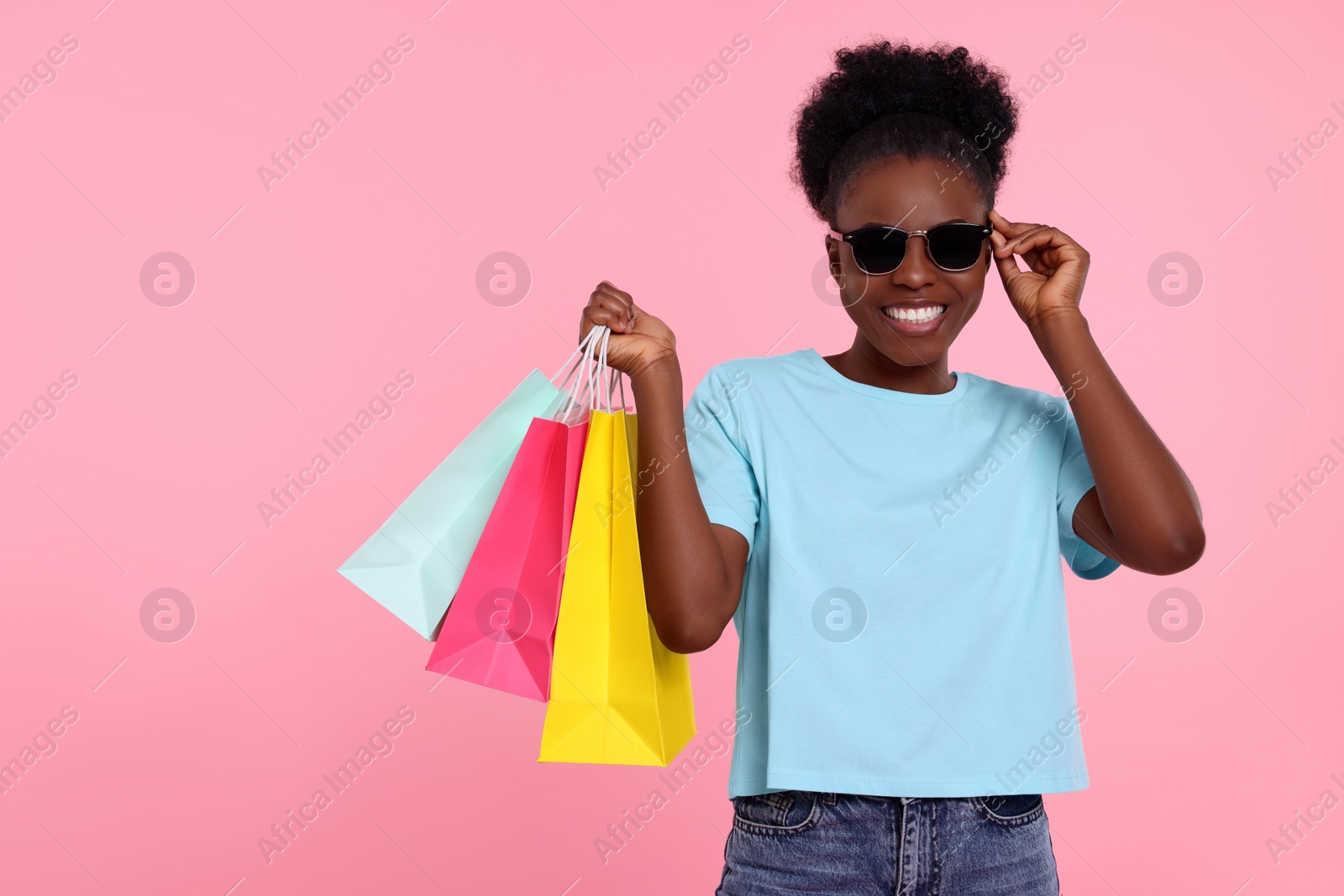 Photo of Happy young woman in stylish sunglasses with shopping bags on pink background. Space for text