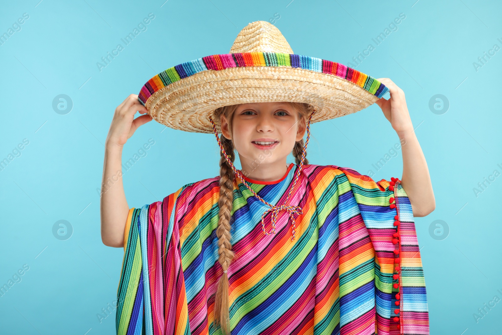 Photo of Cute girl in Mexican sombrero hat and poncho on light blue background