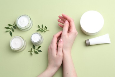 Woman applying hand cream on green background, top view