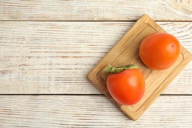 Photo of Tasty ripe persimmons on white wooden table, top view. Space for text