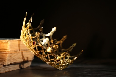 Photo of Beautiful golden crown and old books on black table. Fantasy item
