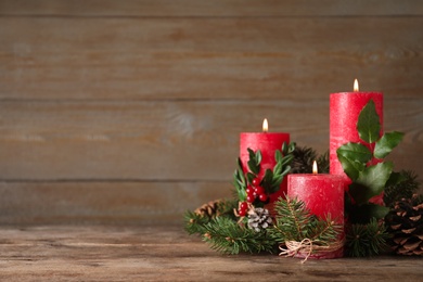 Photo of Burning red candles with Christmas decor on wooden table. Space for text