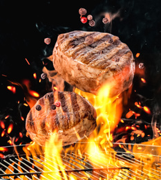 Meat and peppers mix falling onto barbecue grill with flame against black background, closeup