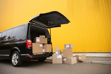 Photo of Black delivery van and many different parcels near yellow building outdoors. Courier service