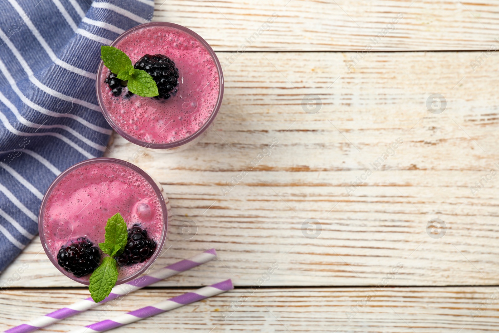 Photo of Glasses of blackberry smoothie with mint and berries on light wooden table, flat lay. Space for text