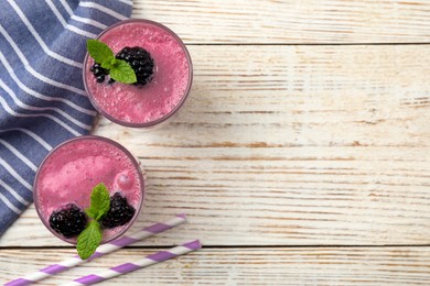 Photo of Glasses of blackberry smoothie with mint and berries on light wooden table, flat lay. Space for text