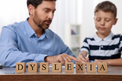 Father helping son with homework and cubes with word Dyslexia at table indoors, selective focus