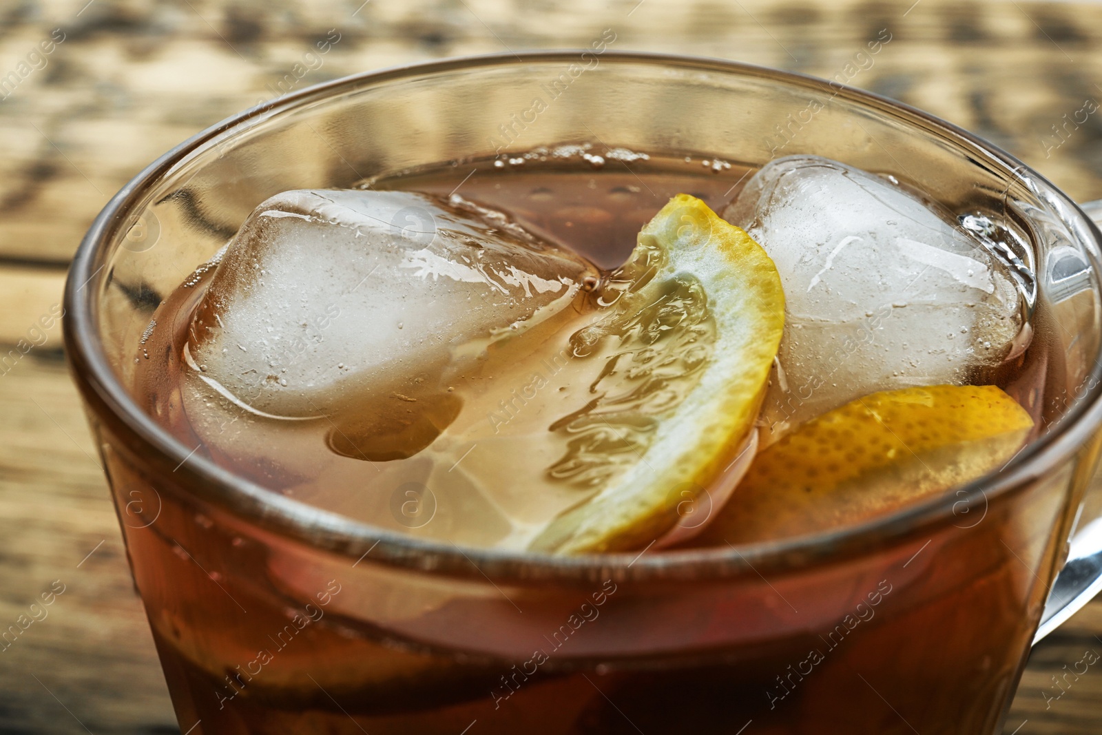 Photo of Cup of delicious iced tea on wooden table, closeup