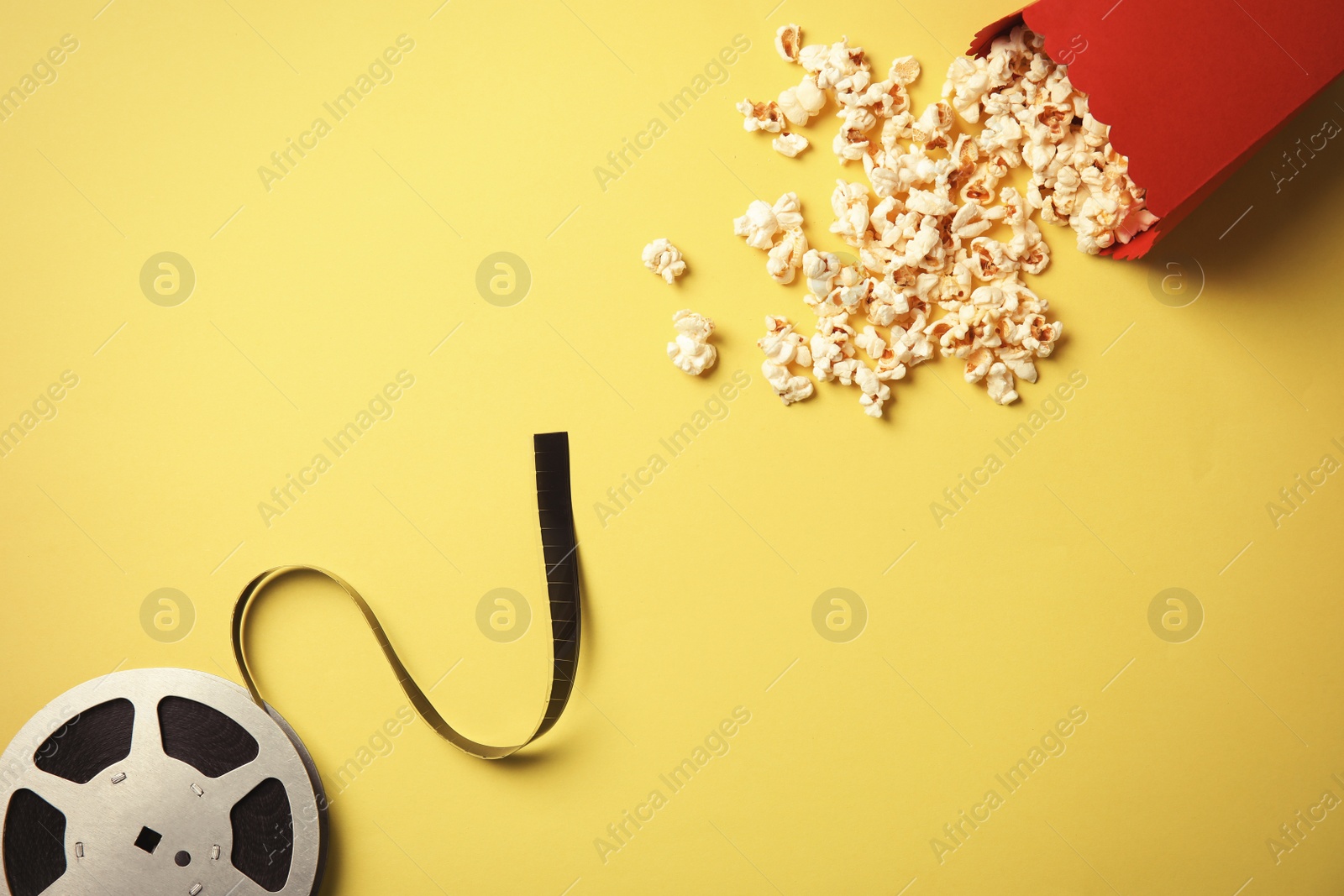 Photo of Tasty popcorn and film reel on color background, top view. Cinema snack