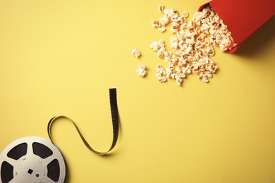 Tasty popcorn and film reel on color background, top view. Cinema snack