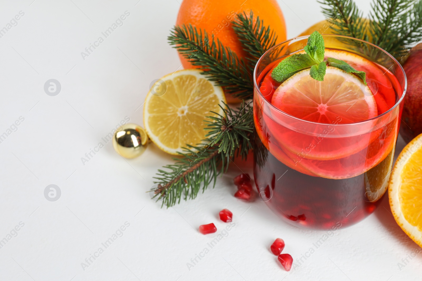 Photo of Christmas Sangria drink in glass, fir branches and fruits on white background, closeup. Space for text