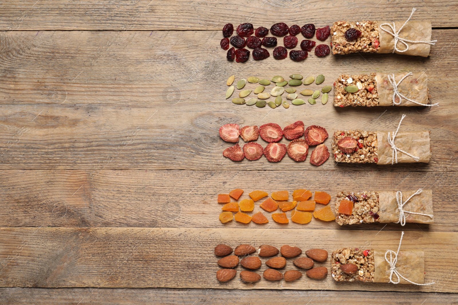 Photo of Different tasty granola bars and ingredients on wooden table, flat lay. Space for text