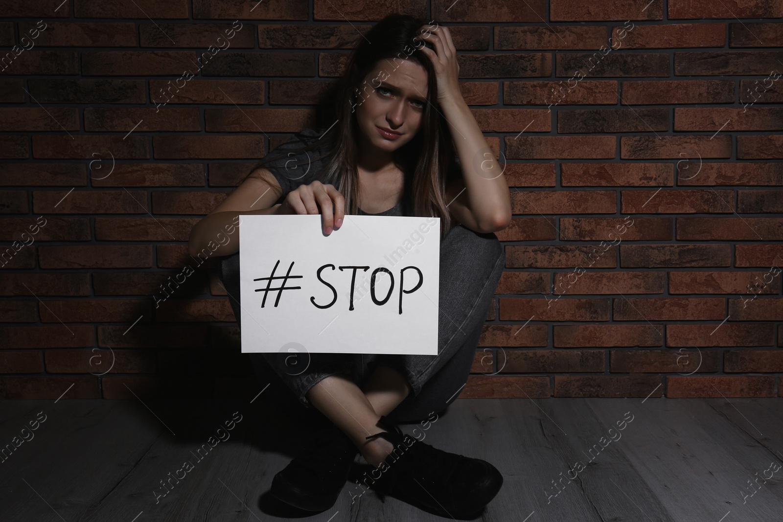 Photo of Crying young woman with hashtag STOP near brick wall. Domestic violence concept