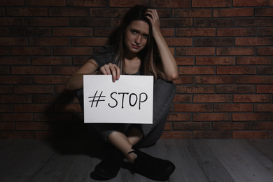 Photo of Crying young woman with hashtag STOP near brick wall. Domestic violence concept