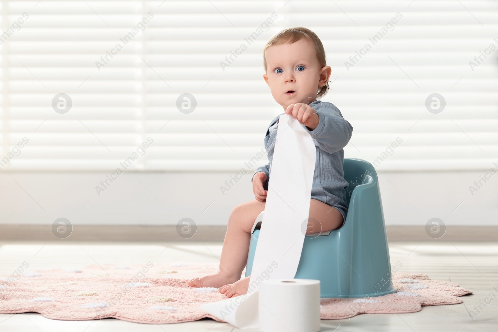 Photo of Little child with toilet paper roll sitting on plastic baby potty indoors. Space for text