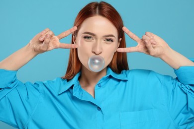 Photo of Beautiful woman blowing bubble gum and gesturing on turquoise background