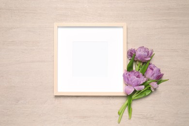 Photo of Empty photo frame and beautiful tulip flowers on wooden background, flat lay. Mockup for design