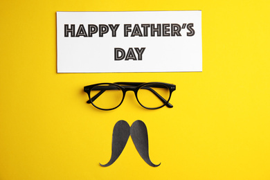 Eyeglasses, paper mustache and card with phrase HAPPY FATHER'S DAY on yellow background, flat lay