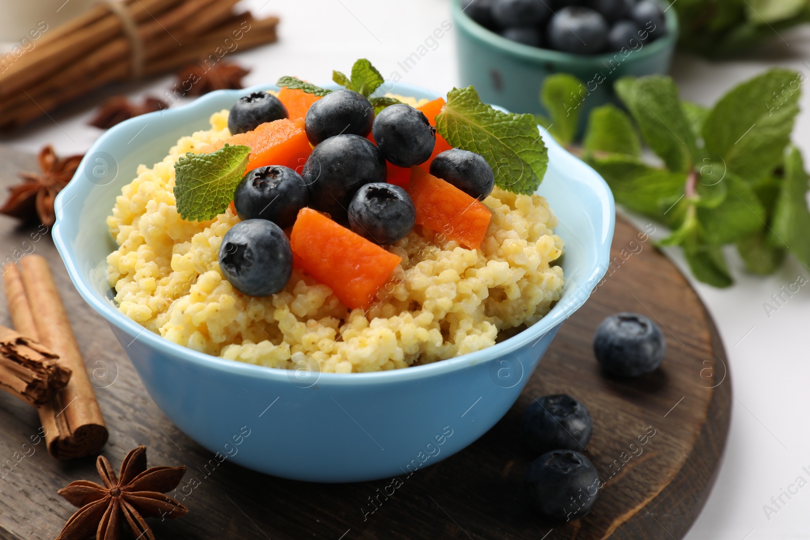 Photo of Tasty millet porridge with blueberries, pumpkin and mint in bowl on white table, closeup