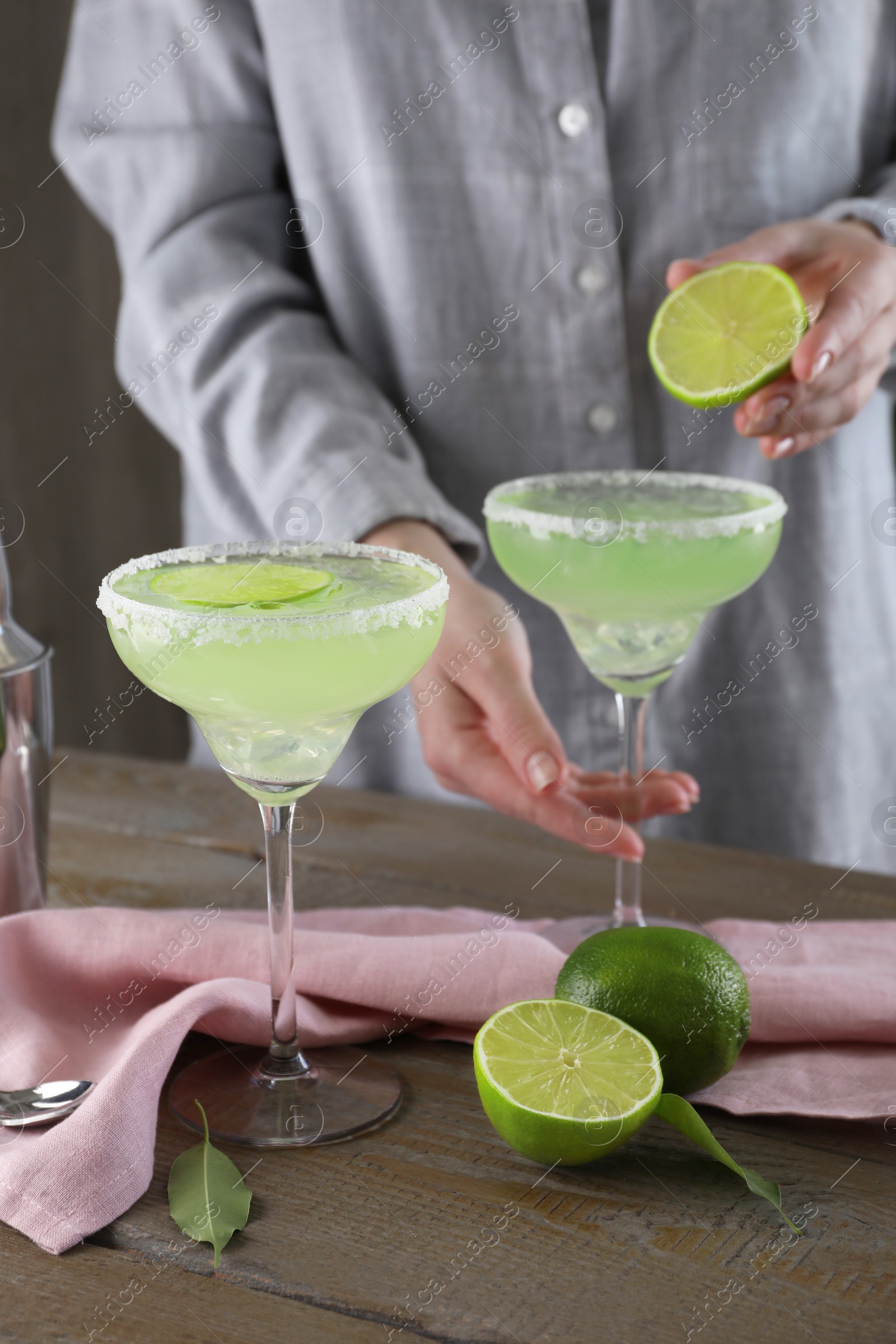 Photo of Woman squeezing lime juice into glass with delicious Margarita cocktail at wooden table, closeup