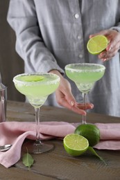 Photo of Woman squeezing lime juice into glass with delicious Margarita cocktail at wooden table, closeup