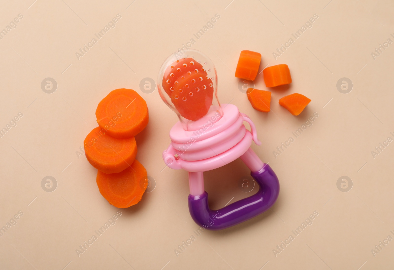 Photo of Nibbler with boiled carrot on beige background, flat lay. Baby feeder