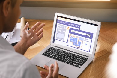 Image of Man working with modern laptop at wooden table indoors, closeup. Job search