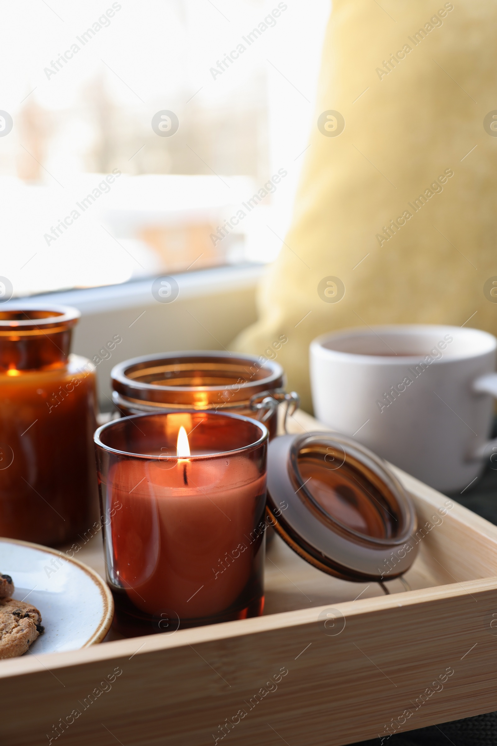 Photo of Tray with burning candles near window indoors