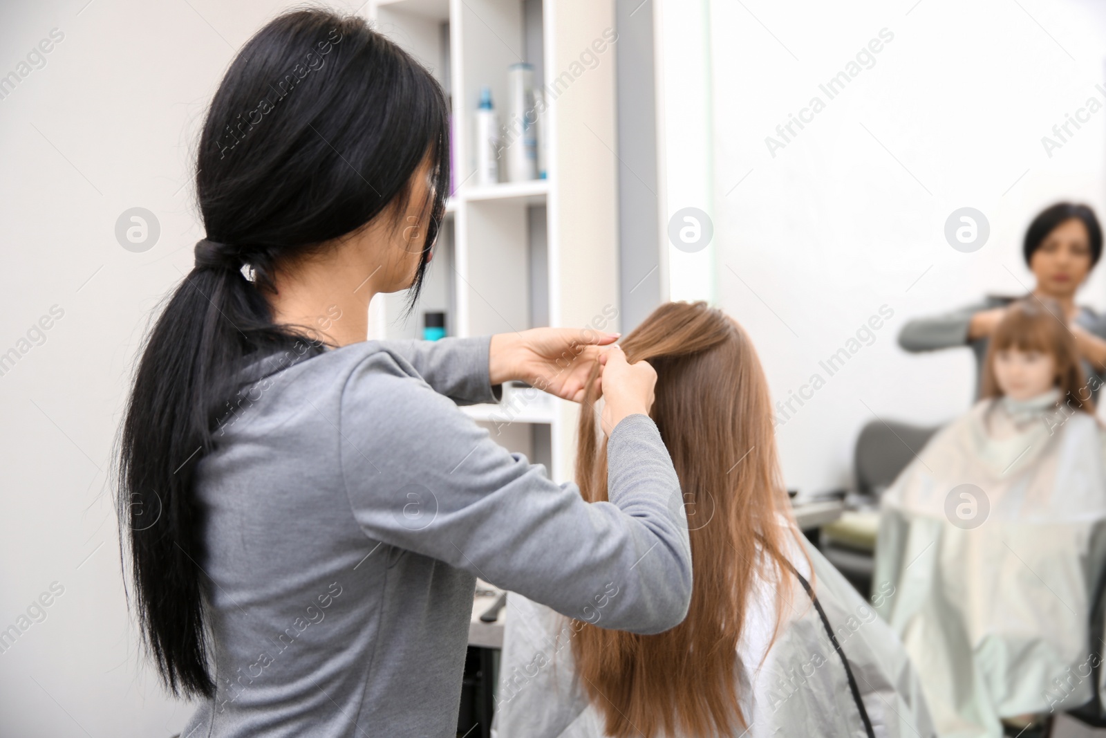 Photo of Professional female hairdresser working with little girl in salon