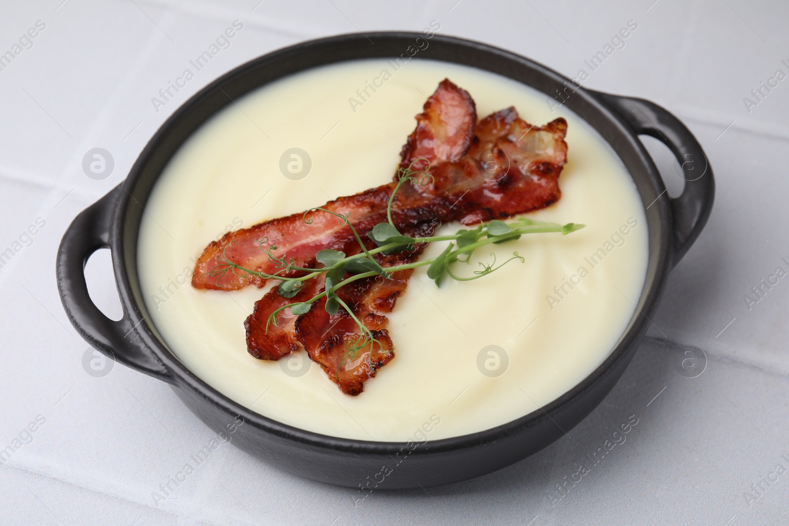 Photo of Delicious potato soup with bacon and microgreens in bowl on white tiled table, closeup