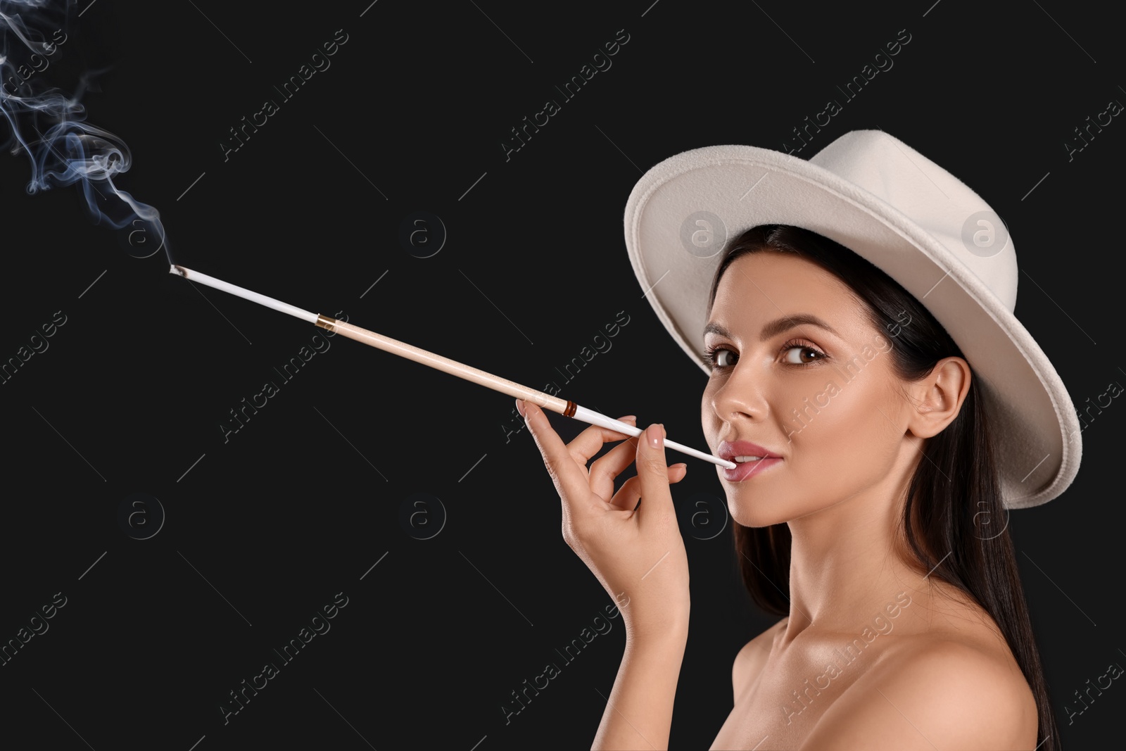 Photo of Woman using long cigarette holder for smoking on black background