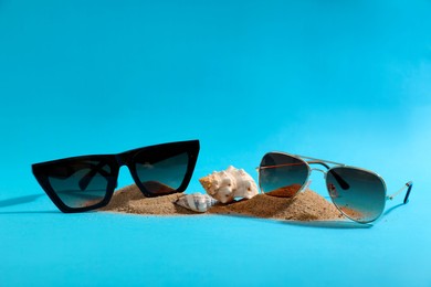 Stylish sunglasses, seashells and sand on light blue background. Space for text