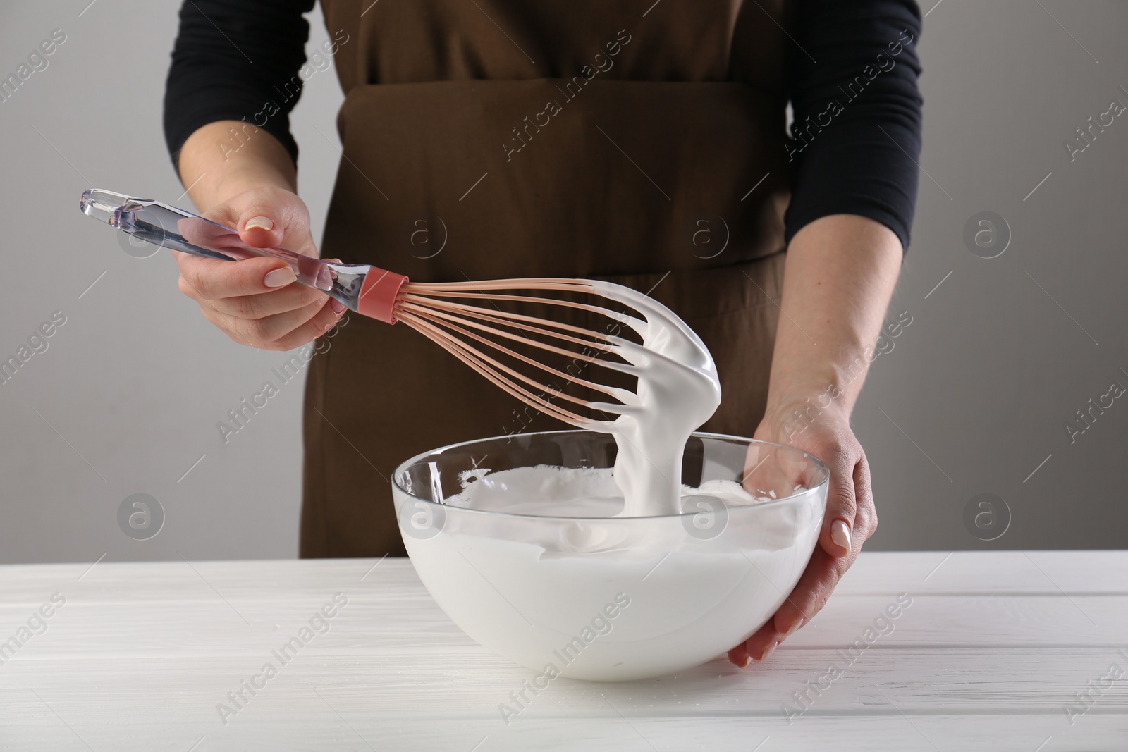 Photo of Woman making whipped cream with whisk at white wooden table, closeup