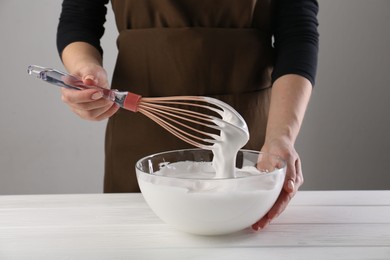 Woman making whipped cream with whisk at white wooden table, closeup