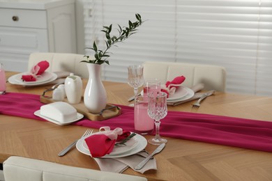 Photo of Color accent table setting. Glasses, plates, pink napkins and vase with green branch in dining room