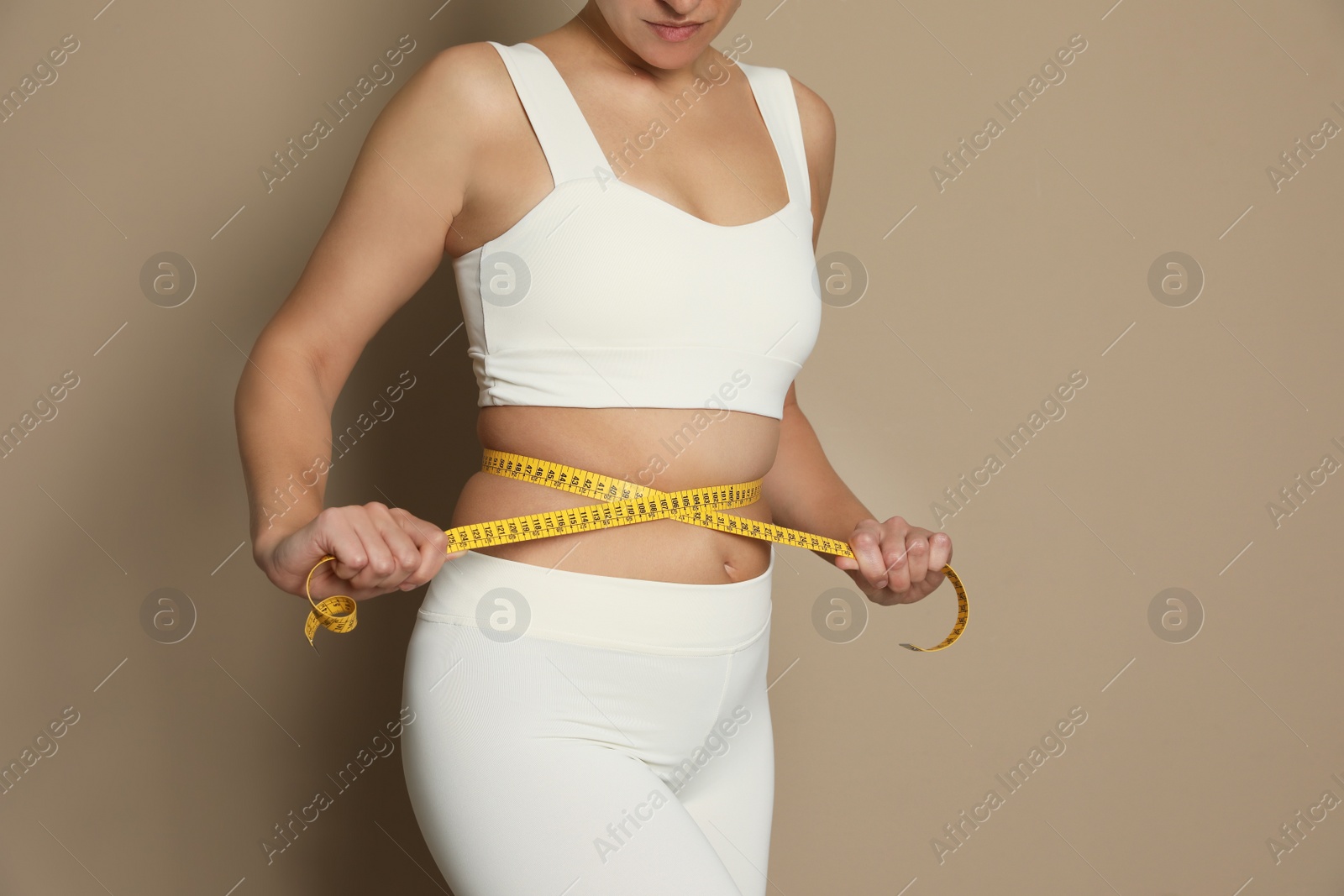 Photo of Woman measuring waist with tape on beige background, closeup