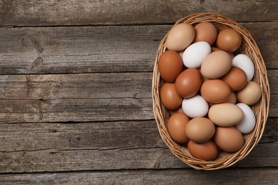Photo of Fresh chicken eggs in wicker basket on wooden table, top view. Space for text